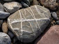 Kreuz und quer weißgebänderter gräulicher Stein